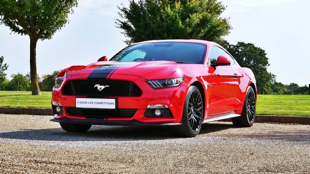 A red Ford Mustang GT parked on a tree-lined drive